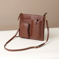 Brown leather crossbody bag on a white surface with a beige background