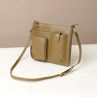 Green handbag with a crossbody strap on a white surface with a beige background