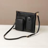 Black leather crossbody bag with a strap on a white surface and beige background