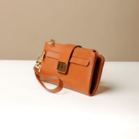 A brown leather wallet with a zipper closure, a detachable wristlet strap, and a brand emblem on the front.