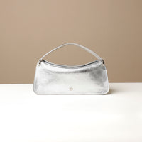A silver, square-shaped leather handbag with a fold-over closure and a magnetic clasp, displayed on a neutral surface.
