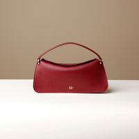 A red, square-shaped leather handbag with a fold-over closure and a magnetic clasp, displayed on a neutral surface.