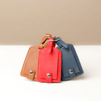 Three leather luggage tags in red, brown, and blue colors, displayed upright with a buckle closure and a tag strap.