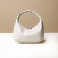A beige, soft rounded handbag with a handwoven strap and a sleek, minimalistic design on a light background.