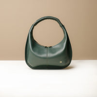 A green, soft rounded handbag with a handwoven strap and a sleek, minimalistic design on a light background.