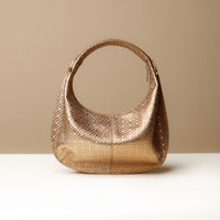 A gold, soft rounded handbag with a handwoven strap and a sleek, minimalistic design on a light background.
