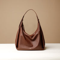 A brown, hobo-style leather handbag with a slouchy silhouette and a minimalist design, displayed against a neutral background.