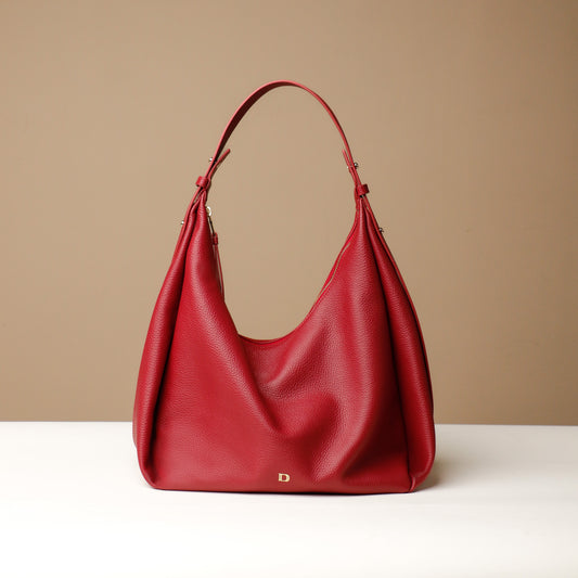 A Red, hobo-style leather handbag with a slouchy silhouette and a minimalist design, displayed against a neutral background.