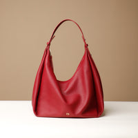 A Red, hobo-style leather handbag with a slouchy silhouette and a minimalist design, displayed against a neutral background.