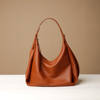A brown, hobo-style leather handbag with a slouchy silhouette and a minimalist design, displayed against a neutral background.
