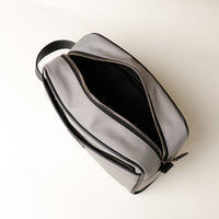 A gray toiletry bag with black trim being held open, displaying its interior compartments