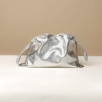 Silver metallic handbag with chain strap on a beige background