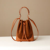 A brown suede bucket bag with a drawstring-style tie closure and a flat sole.