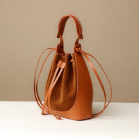 A brown suede bucket bag with a drawstring-style tie closure and a flat sole.