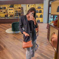 Person holding a brown handbag in a store with various bags on display.