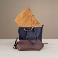 Three leather handbags in blue, brown, and tan on a neutral background