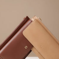 Close-up of two leather wallets, one brown and one beige, on a neutral background.