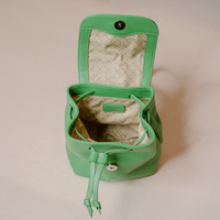 A mint green leather bucket bag shown open, displaying its patterned beige interior lining and drawstring closure, set against a solid beige background.
