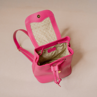 A bright pink leather bucket bag with an open top, showing a beige patterned interior lining and a matching pink shoulder strap, photographed on a plain beige background.