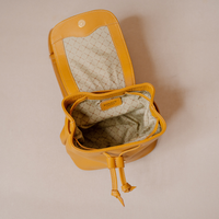 A mustard yellow leather bucket bag shown open from a top-down view, revealing a cream-colored patterned interior lining and a drawstring closure.