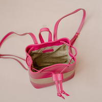 A bright pink leather bucket bag with a beige and pink striped base, shown from an overhead angle on a light beige background.