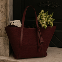 Brown leather tote bag with a plant and books on a stone surface. Isola mesh tote bag with leather trims