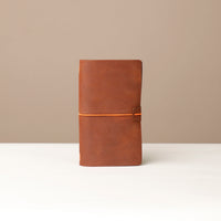 A brown leather journal with a orange elastic band on a white surface.
