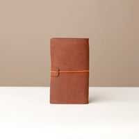 Front View A brown leather journal with a orange elastic band on a white surface.