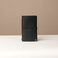 A black leather journal with a black elastic band on a black surface.