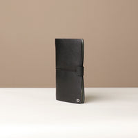 Angled View of A black leather journal with a black elastic band on a black surface.