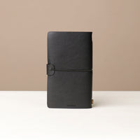 Close Up View of A black leather journal with a black elastic band on a black surface.