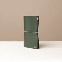 Angled View of A Green leather journal with a silver elastic band on a leather surface.