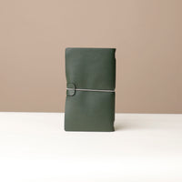 Front View of A Green leather journal with a silver elastic band on a leather surface.