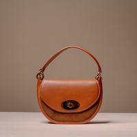 A structured tan leather handbag with a curved top handle, a front flap, and a gold-tone turn-lock closure, photographed against a neutral beige background.