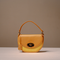 A yellow leather shoulder bag with a herringbone-patterned yellow mesh front panel and gold-tone hardware, displayed on a neutral beige background.