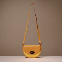 A mustard yellow leather crescent-shaped shoulder bag with a textured mesh lower half and a gold-tone turn-lock closure, displayed on a neutral beige background.