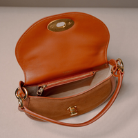 An open tan leather shoulder bag with gold-tone hardware, a zippered interior pocket, and a curved top flap, photographed on a neutral light gray background.