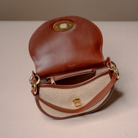 A brown leather and woven beige shoulder bag with gold-tone hardware, shown open against a neutral beige background.