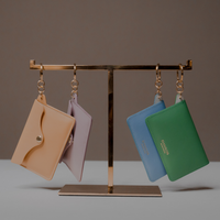 Four colorful Loop Pouch by Danilos in premium leather with key ring hanging on a gold stand against a brown background