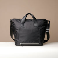 Black travel bag with a shoulder strap on a beige background
