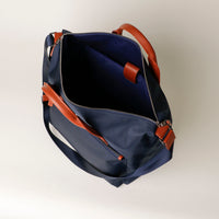 Navy blue bag with brown leather straps on a light gray background