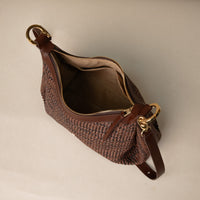Open view of a Mia 26 Raffia Palisander brown handcrafted with raffia and premium leather, with gold hardware and a leather strap, in a beige background
