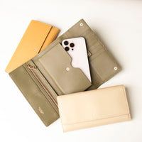 Three leather wallets in beige, green, and yellow colors, with one of them opened to show the interior and a smartphone placed inside.