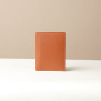 A closed brown leather passport case against a neutral background.