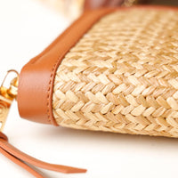 Close-up of a woven handbag with brown leather accents on a white background
