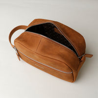 A suede tan toiletry bag 2014 with a silver zipper closure and a handle,placed against a neutral background.  Open view. 