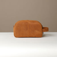 A suede tan toiletry bag 2014 with a silver zipper closure and a handle, placed against a neutral background. Back view. 