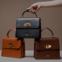 Three Nelda Bag elegant leather handbag with detachable shoulder strap in black, brown, and orange with gold clasps on a neutral background.