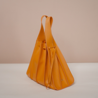 A mustard yellow leather shoulder bag with a slouchy, pleated triangular silhouette and dual top handles, shown on a neutral beige and white background.