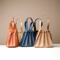Five leather Papillon bags in beige, blue, and brown colors, featuring a bucket silhouette with pleated details and a drawstring closure.